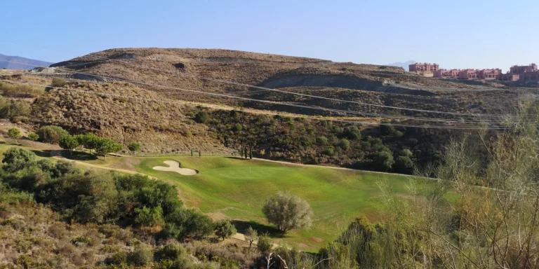 Golf hole in a valley below a dry, terraced hillside