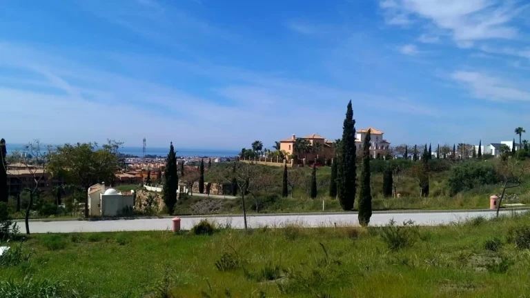 Grassy plot by a road, with cypress trees, Mediterranean-style villas and the sea in the distance