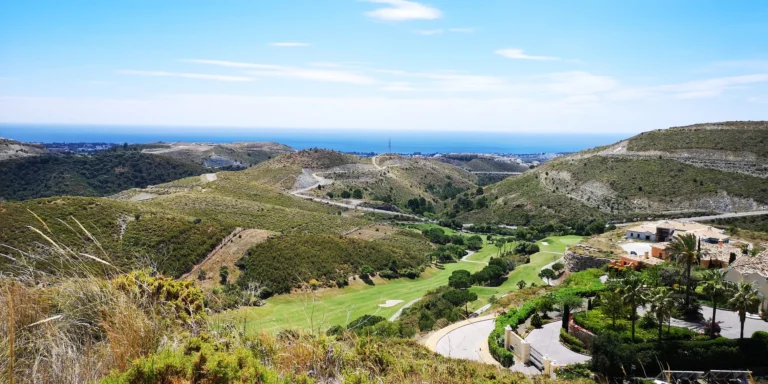 Golf fairway in a valley between dry hills, with the sea on the horizon