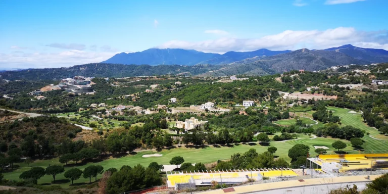 Wide view over a green golf valley dotted with villas, with mountains behind