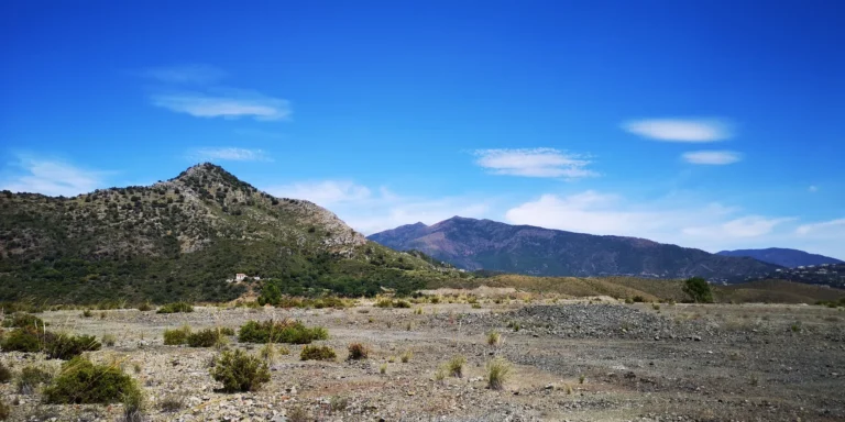 Scrub-covered plateau below a rocky hill, with mountain ridges behind